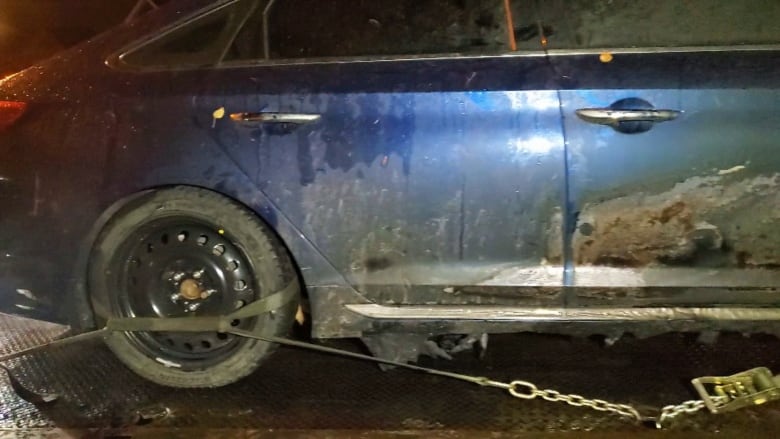 O mașină albastră arsă grav este legată de patul unui camion de remorcare.
